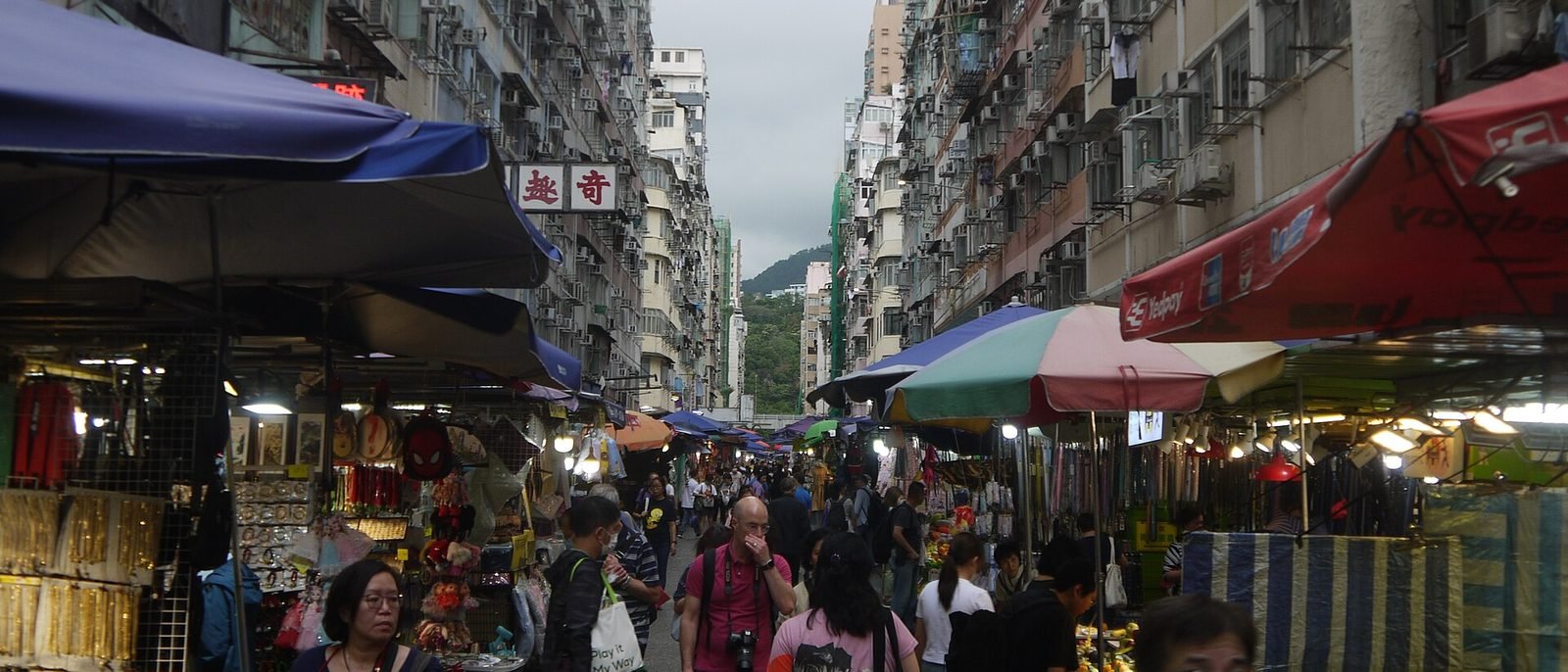 Fa Yuen Street's covered market in Mong Kok by day, awning-covered stalls and a crowd of shoppers under a corridor of tenement towers.
