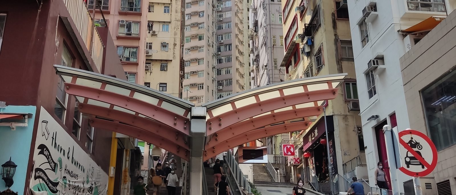 Queen's Road West at its junction with Centre Street in Sai Ying Pun, old tenement facades stacked with air-conditioner units above a taxi waiting at the crossing.