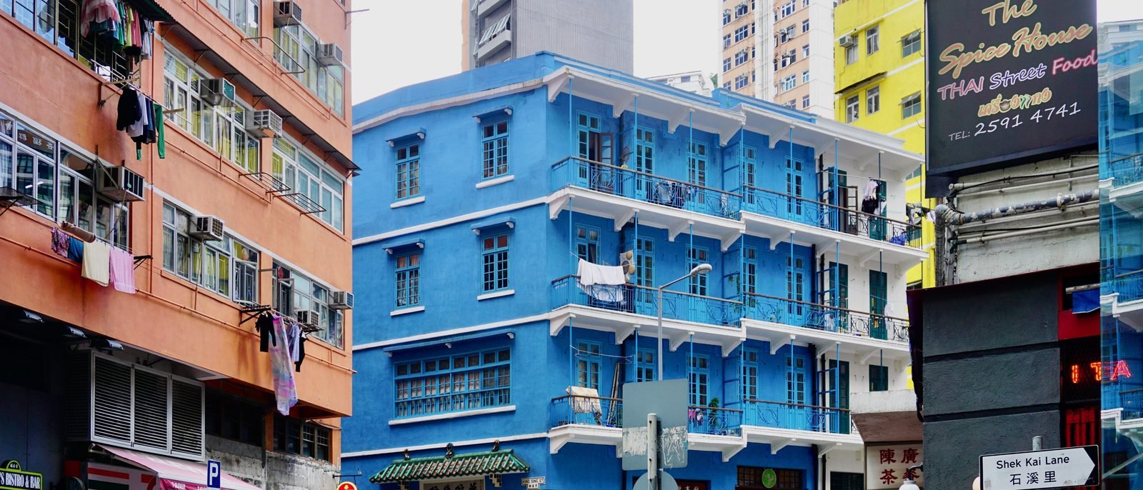 A pink pre-war tong-lau on the corner of Queen's Road East in Wan Chai, a 7-Eleven and a safe shop at street level below older tenement blocks.